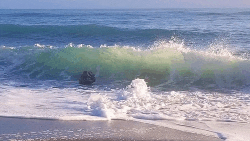 waves crashing on a beach with a large rock in the water