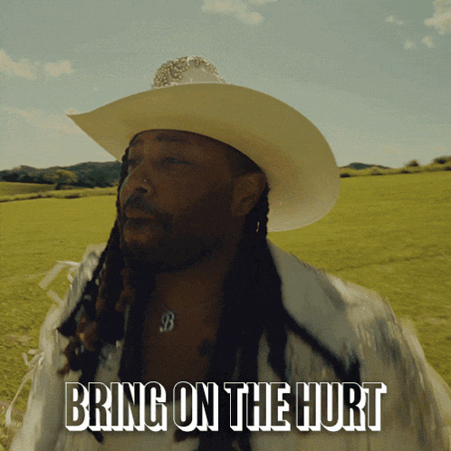 a man in a cowboy hat is standing in a field with the words bring on the hurt below him