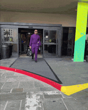 a man in a purple suit walks into a building