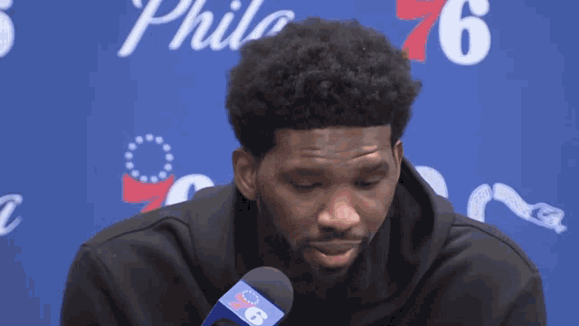 a man speaking into a microphone with a philadelphia 76 logo in the background