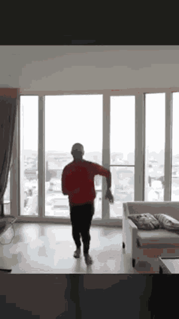 a man in a red sweater is dancing in a living room with a view of a city .