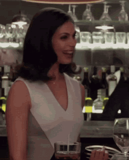 a woman in a white top is sitting at a bar holding a glass