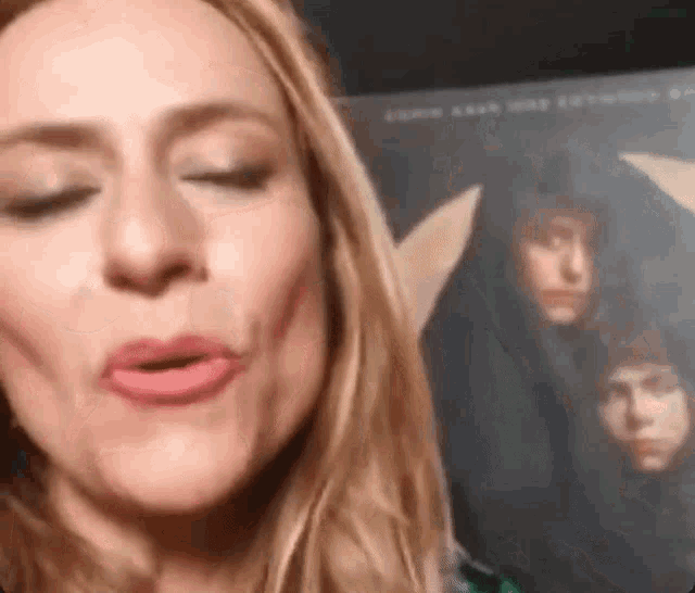 a woman with long blonde hair is making a funny face in front of a picture of two women .