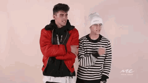 two young men are standing next to each other in front of a pink background .