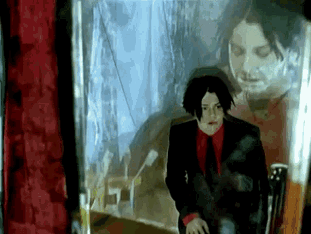 a man in a suit and tie is sitting in front of a mirror with his reflection behind him