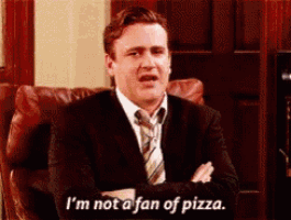 a man in a suit and tie is sitting in a chair and says i 'm not a fan of pizza