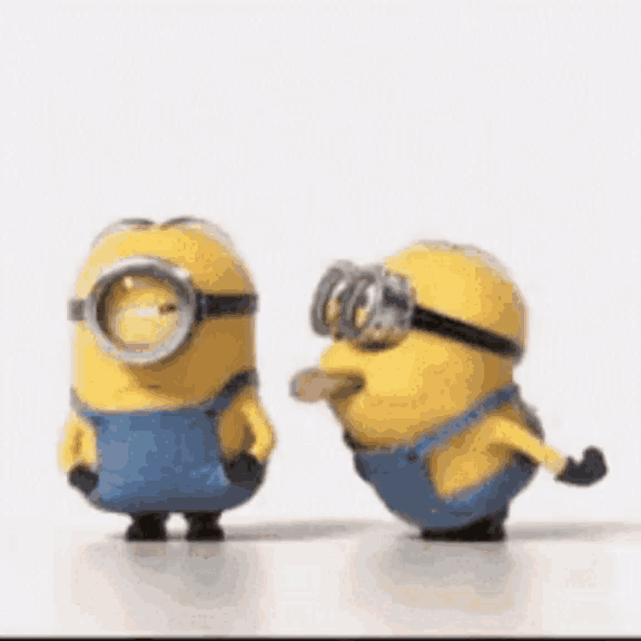 two minions wearing goggles and overalls are standing next to each other on a table .