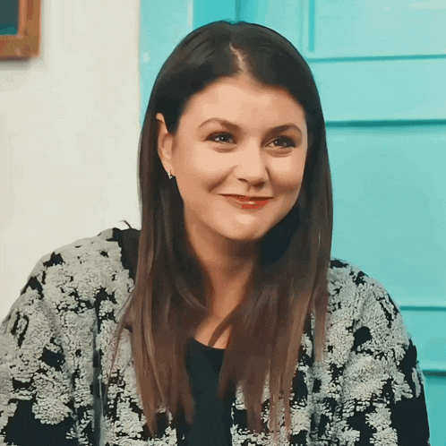 a woman wearing a black and white sweater is smiling in front of a blue door
