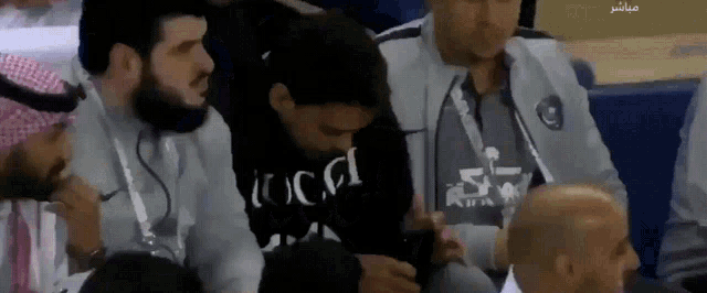 a man wearing a black gucci sweatshirt sits in a crowd
