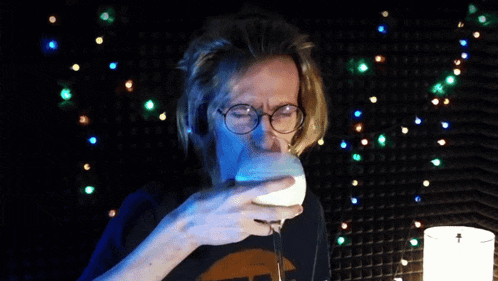 a man with glasses is holding a wine glass with a blue liquid in it