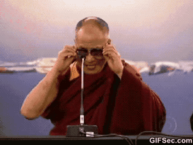 a man adjusts his sunglasses in front of a microphone with gifsec.com at the bottom of the screen
