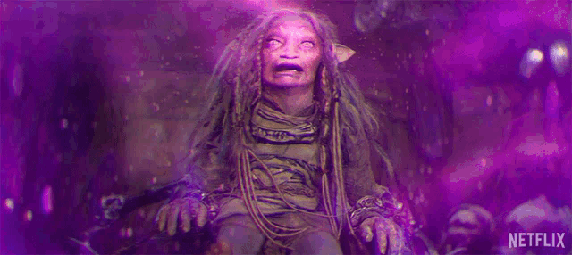 a statue of a woman with dreadlocks is sitting on a rock with a purple background .