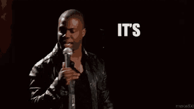 a man in a leather jacket stands in front of a microphone with the words it 's about to go down behind him