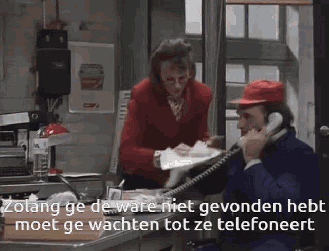 a man in a red hat is talking on a phone with a woman behind him