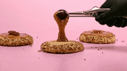 a person in black gloves is pouring caramel onto a cookie