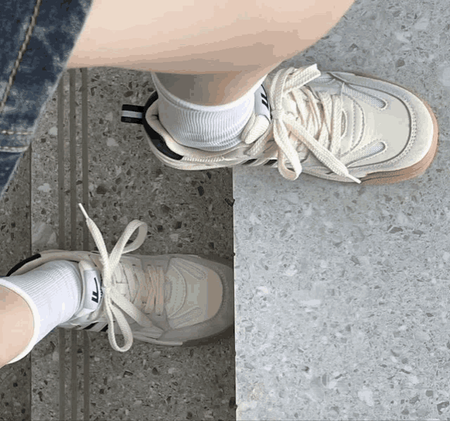 a person wearing a pair of white sneakers with a brown sole