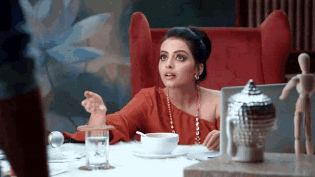 a woman in a red top sits at a table with a cup of coffee