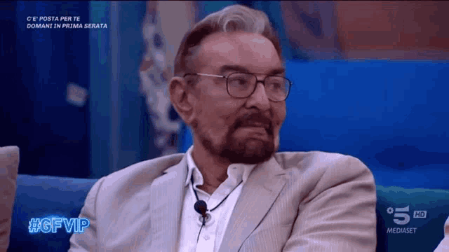a man with glasses and a beard is sitting on a blue couch in front of a screen that says #gfvip