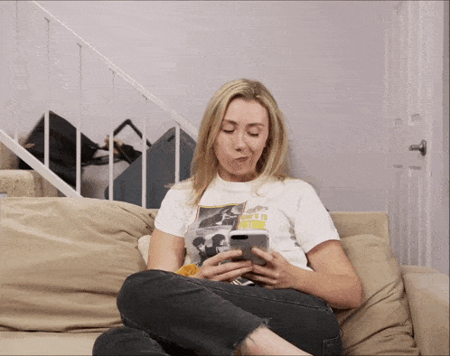 a woman sitting on a couch looking at her phone and wearing a t-shirt that says the beatles