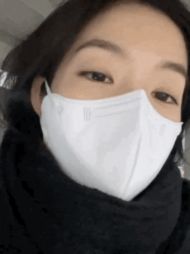 a woman wearing a white mask and a black scarf around her neck
