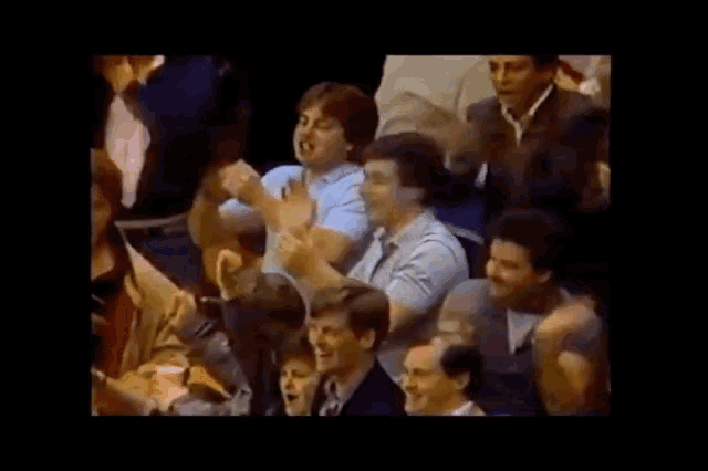 a group of people are sitting in a dark room with their hands up