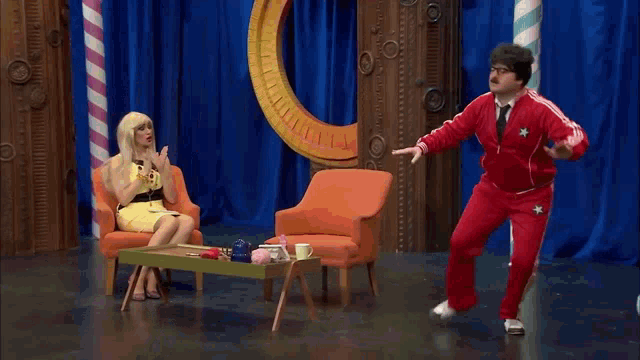 a group of people are sitting in chairs on a stage with a man in a red adidas jacket
