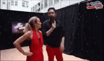 a woman in a red dress is standing next to a man holding a microphone in front of a black curtain .
