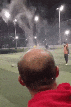 a bald man in a red shirt watches a soccer game