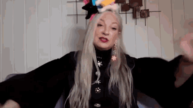 a woman with long blonde hair wearing a black sweater and earrings is sitting on a couch .