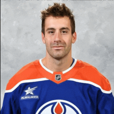 a man wearing a playalberta jersey stands in front of a grey background