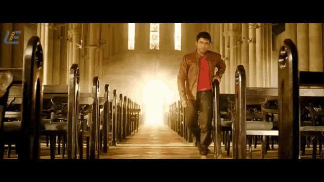 a man in a red shirt stands in an empty church with the letter l behind him