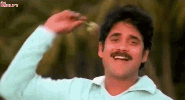 a man with a mustache is smiling and waving his hand in the wind .