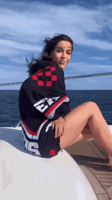 a woman is sitting on a boat wearing a black and red shirt with the letter e on it
