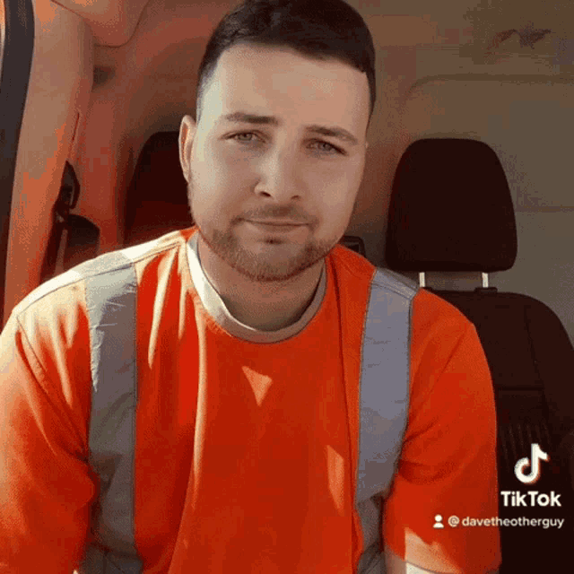 a man wearing an orange shirt and safety vest is sitting in a car with tiktok written on the bottom right corner