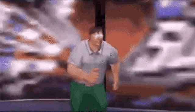 a man in a gray shirt and green pants is standing in front of a wall .