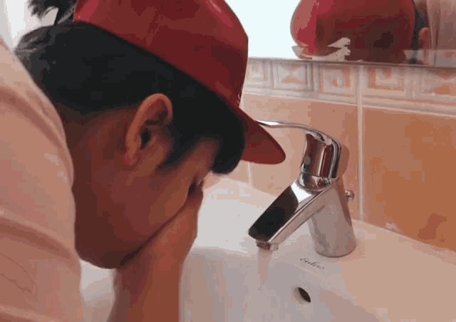 a person wearing a red hat is washing their face in the sink