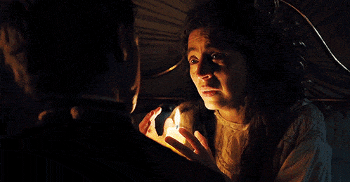a woman holds a lit candle in front of a man in a dark room