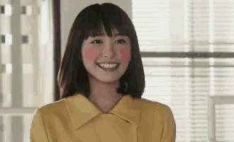 a woman in a yellow jacket is smiling with her blush on her cheeks and looking at the camera .