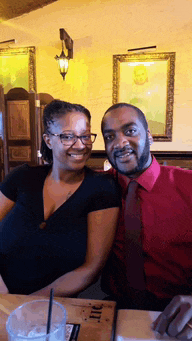a man in a red shirt and tie sits next to a woman with glasses