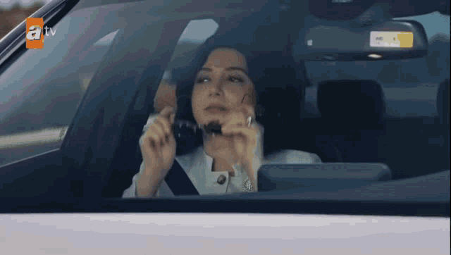 a woman is sitting in a car with a tv logo on the bottom right