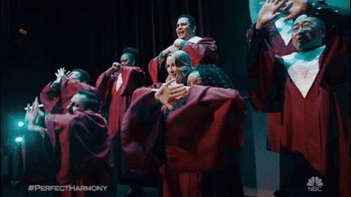 a group of men in red gowns are performing on a stage with the nbc logo in the corner
