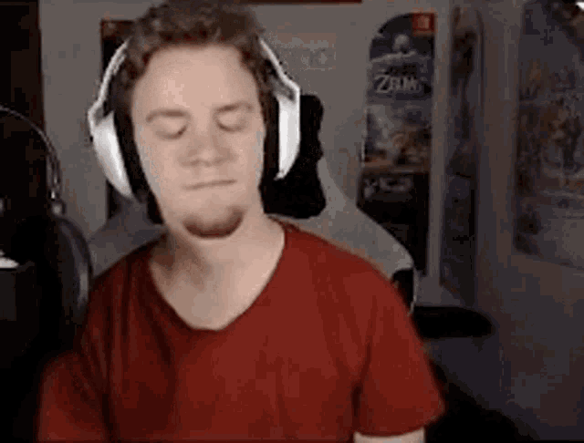 a man wearing headphones and a red shirt is sitting in front of a microphone with his eyes closed .