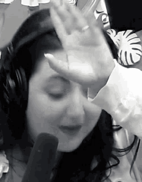 a woman covering her face with her hand while wearing headphones and a white shirt