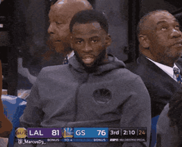 a man sitting in the stands watching a basketball game with the score lal 81 gs 76