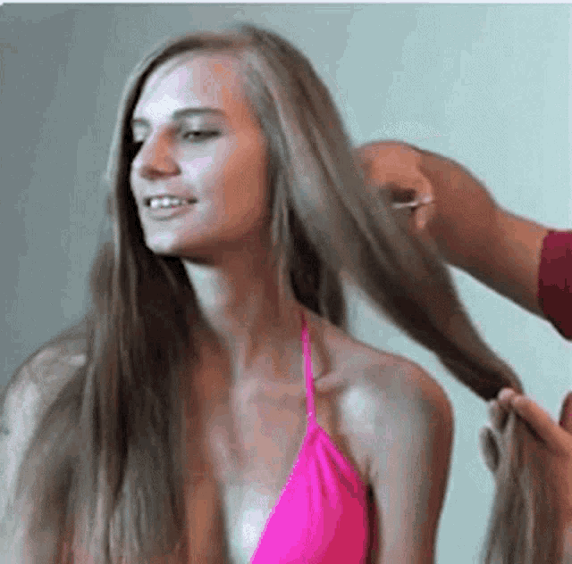 a woman in a pink bikini top is getting her hair braided .