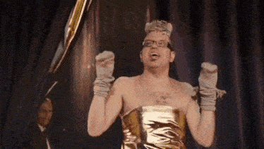 a shirtless man in a gold dress is standing on a stage .