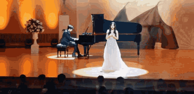 a woman in a white dress is singing while a man plays the piano