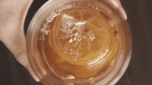 a person is holding a glass with a slice of orange in it