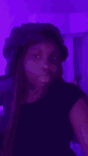 a woman wearing a black hat is taking a selfie in front of a purple light