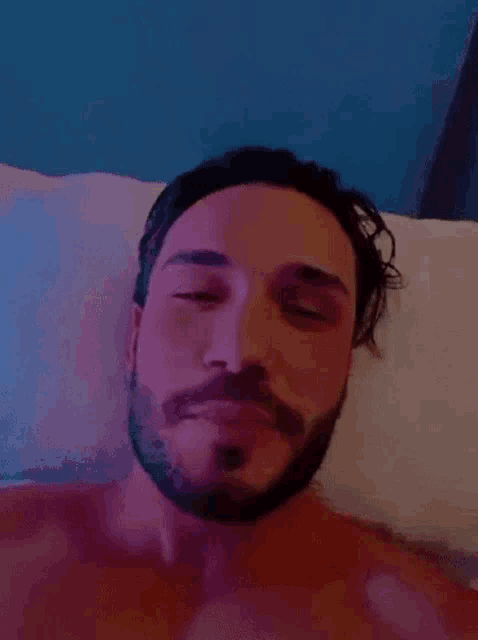 a shirtless man with a beard is laying on a bed and smiling .